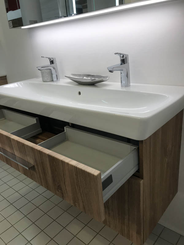 Doppel-Waschbecken in weiß Armaturen in Chrom Unterschrank in Holzoptik dunkel geöffnete Schublade Seitenansicht